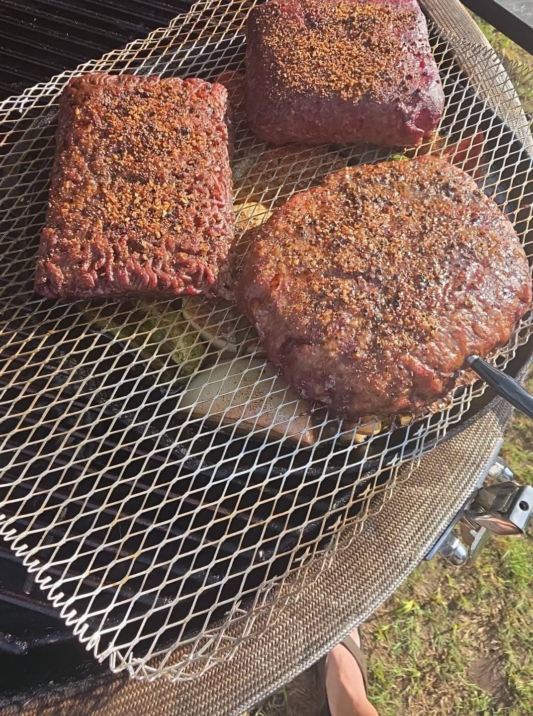 Magic Cow Dust–seasoned beef and bison smoking on a rack above the vegetable catch pan.